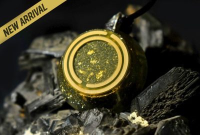 Μενταγιόν Pyrite Fire με μεταλλική χρυσαφένια λάμψη, κρεμασμένο σε μαύρο κορδόνι. Εικονίζεται σε φυσικό φως, επάνω σε σκούρα πέτρα – συμβολίζει την εσωτερική φλόγα, την προστασία και τη χαρά.